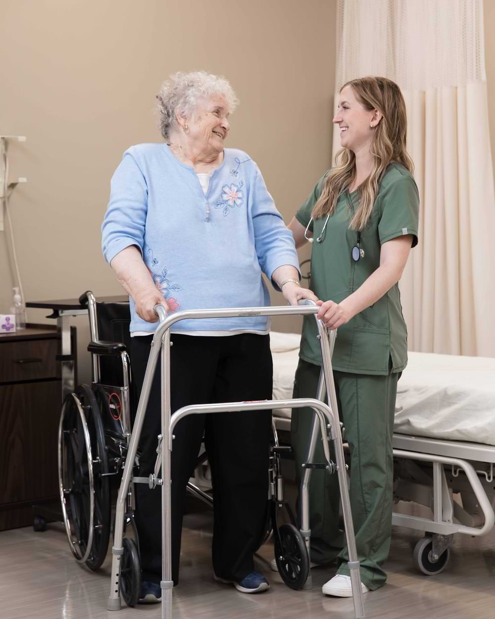 A student wearing scrubs standing next to a patient using a walker