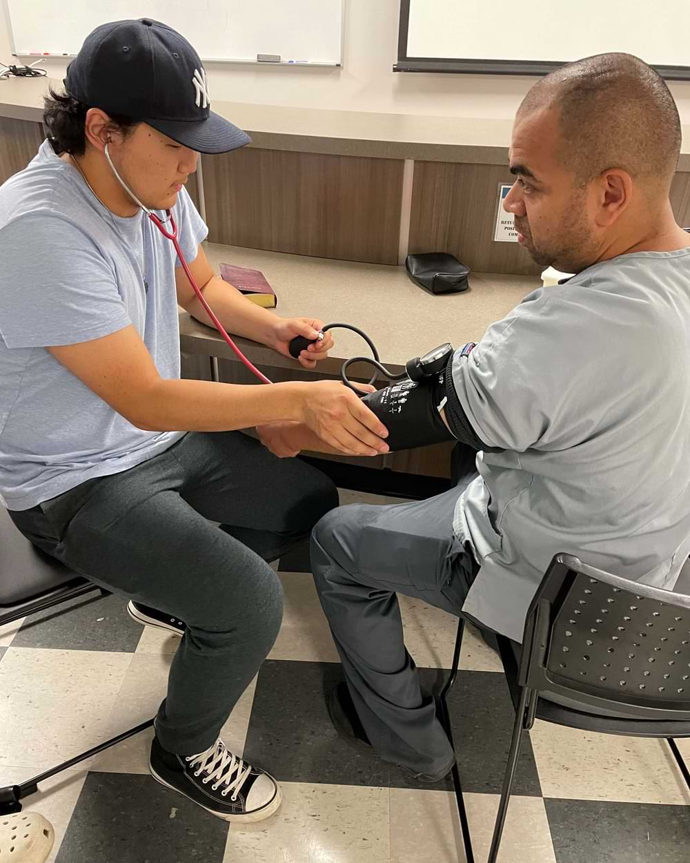 Man in a baseball cap taking the blood pressure of a male patient